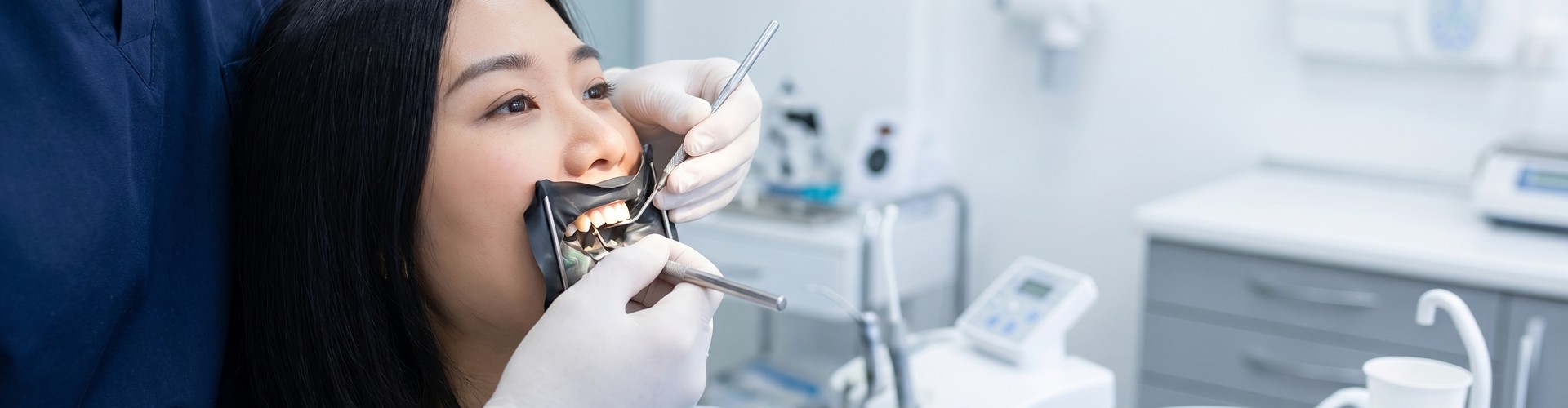 Gloved hands using dental tools in woman's mouth.